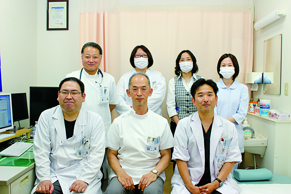 外科担当の医師とスタッフ。前段左から小坂芳和医師、髙井昭洋医師、山元英資医師、後段左の田中仁医師のほか、松山医療福祉センター長補佐の安岡康夫医師がおり、5人の常勤医師が在籍（2021年8月現在）。全員が外科専門医（日本外科学会認定）